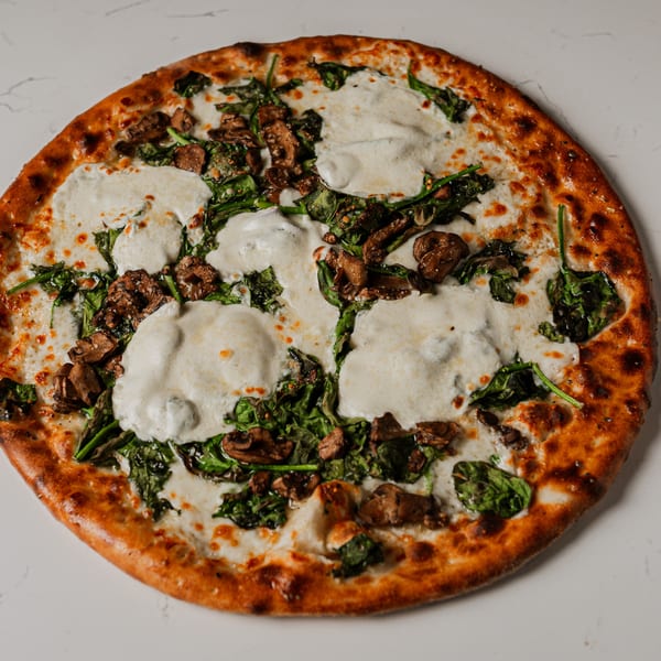 Pazza Pizza's white pizza with fresh mozzarella, spinach, and mushrooms on a white surface.