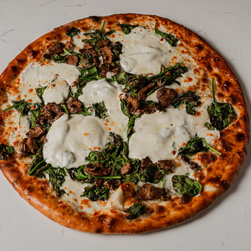 Pazza Pizza's white pizza with fresh mozzarella, spinach, and mushrooms on a white surface.