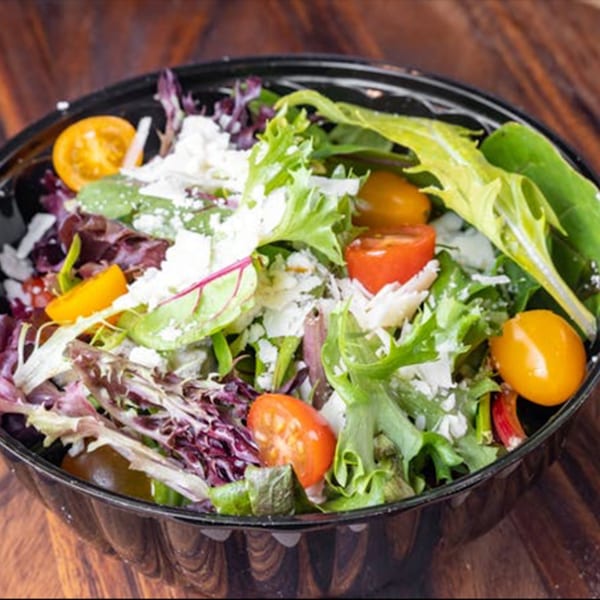 Fresh Pazza Pizza house salad with mixed greens, cherry tomatoes, and crumbled cheese in a black bowl.