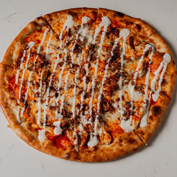 A whole Pazza Pizza with red sauce, cheese, chicken, bacon, and a white drizzle.