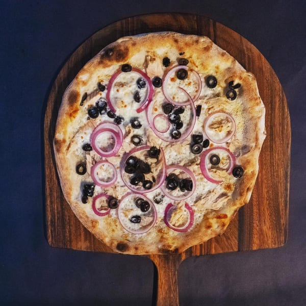 Pazza Pizza's white pizza with red onions and black olives on a wooden pizza peel.
