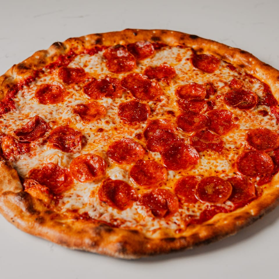 A whole pepperoni pizza from Pazza Pizza, with melted cheese and a golden-brown crust.