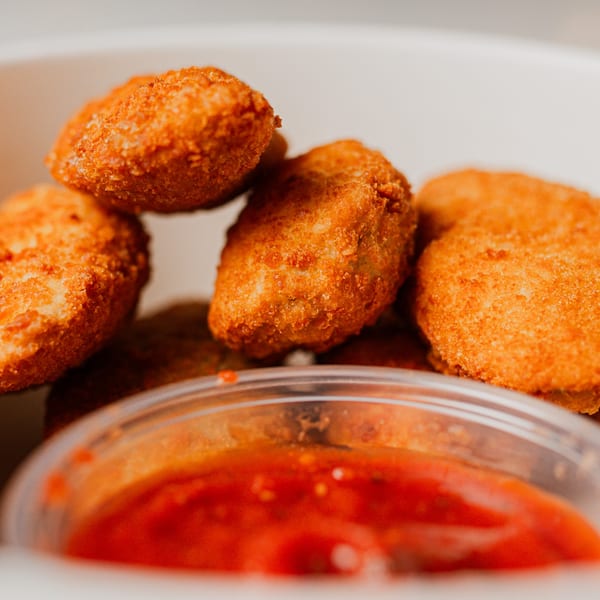 Golden-brown fried nuggets are piled next to a small container of red marinara dipping sauce.
