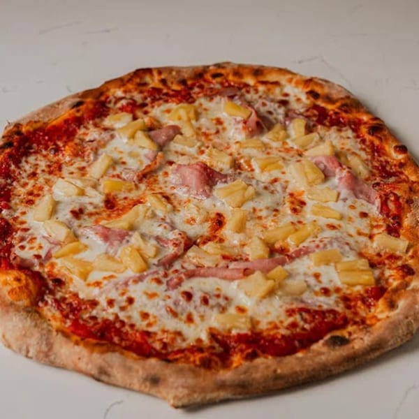 Pazza Pizza's Hawaiian pizza, topped with ham, pineapple, and melted cheese on a white surface.