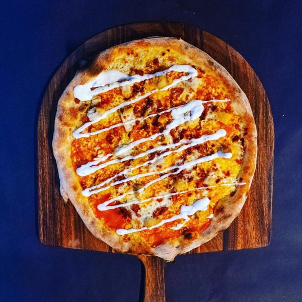 Pazza Pizza's pizza with red sauce, cheese, and white sauce drizzle on a wooden peel.