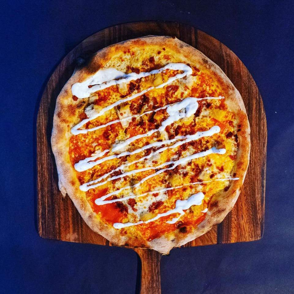 Pazza Pizza's pizza with red sauce, cheese, and white sauce drizzle on a wooden peel.