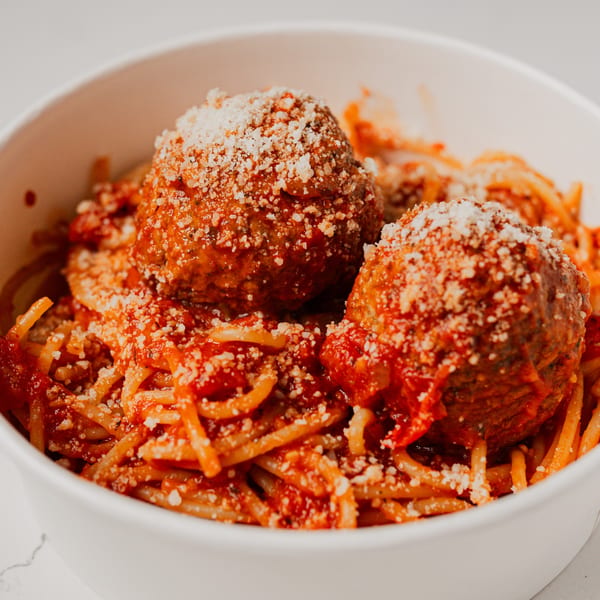 Spaghetti and meatballs with marinara sauce and grated cheese in a white bowl.