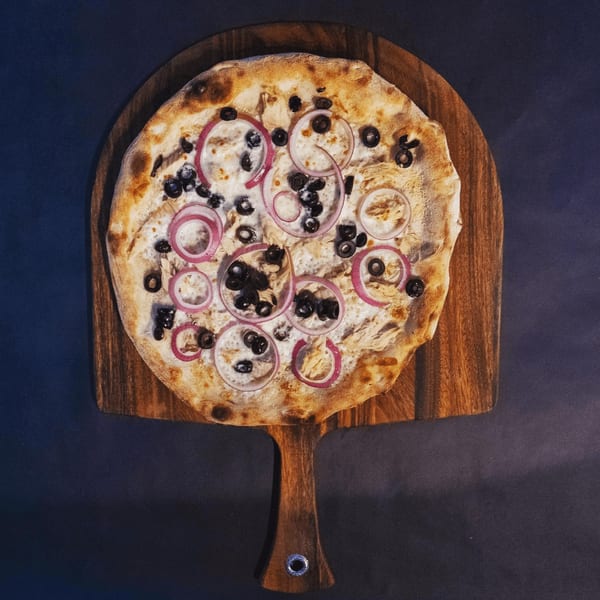Pazza Pizza's white pizza with red onion and black olives on a wooden peel.