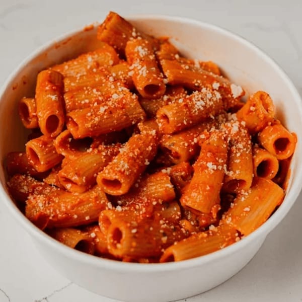 Rigatoni pasta with red sauce and grated cheese in a white bowl from Pazza Pizza.