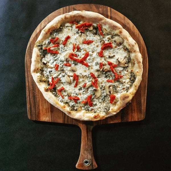 Pazza Pizza's white pizza with mushrooms and sun-dried tomatoes on a wooden peel.