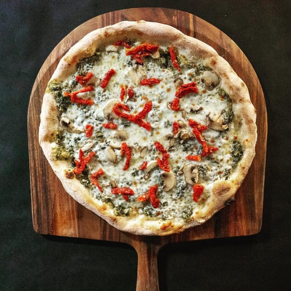 Pazza Pizza's white pizza with pesto, mushrooms, and sun-dried tomatoes on a wooden peel.