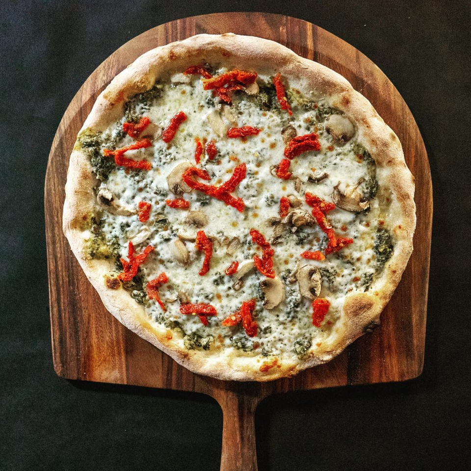 Pazza Pizza's white pizza with pesto, mushrooms, and sun-dried tomatoes on a wooden peel.